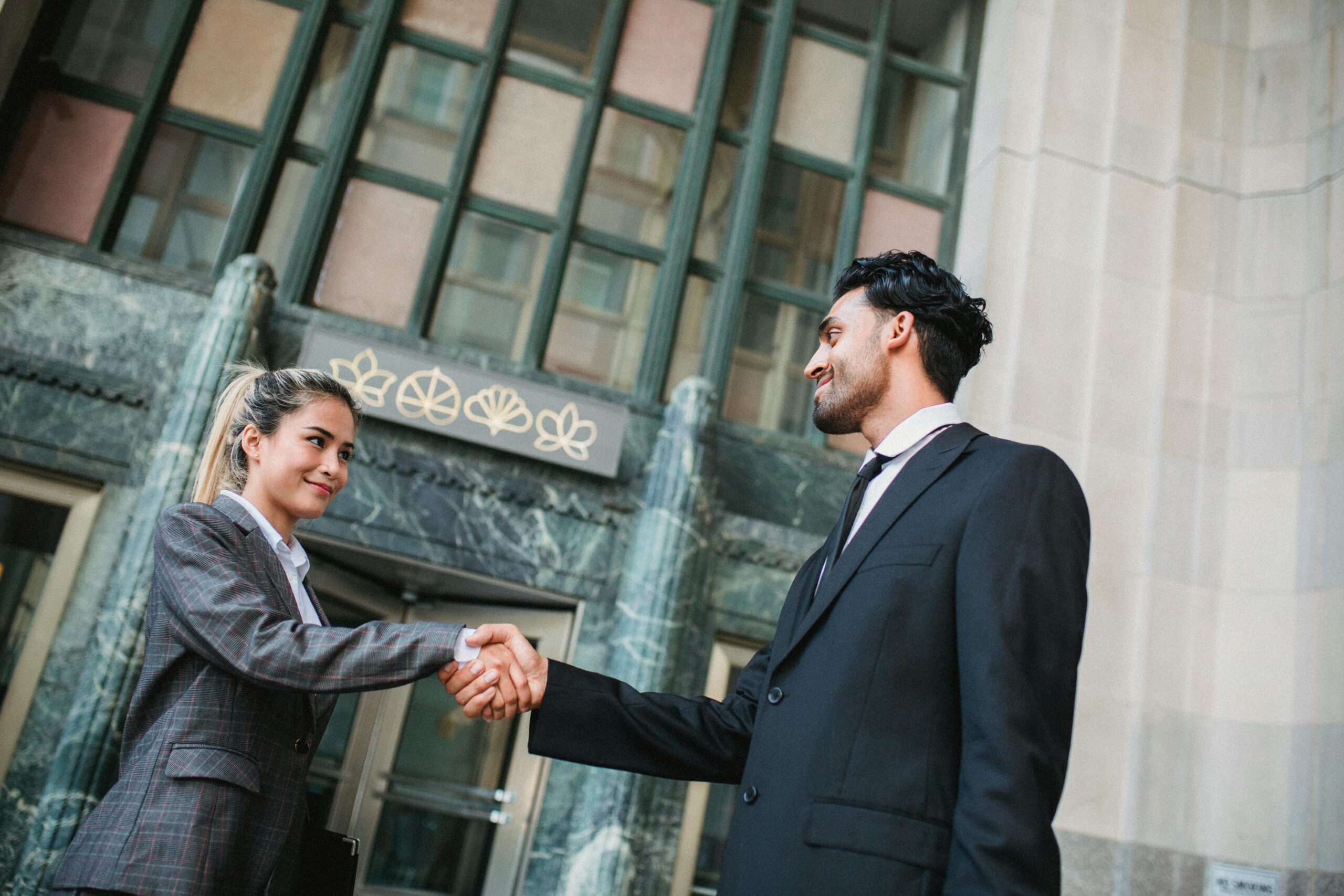 Two business professionals exchanging a handshake outside an office building.
