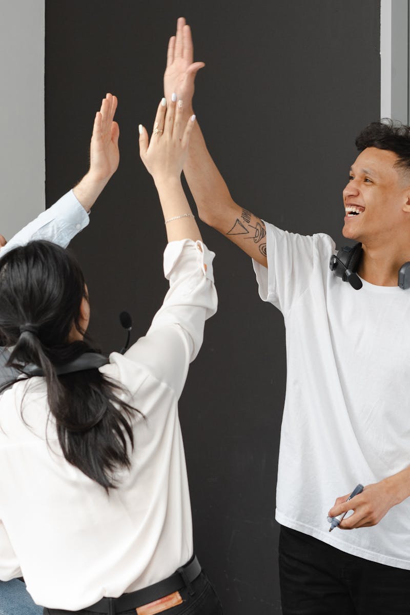 Diverse team members in an office high-fiving, symbolizing success and teamwork in a supportive environment.